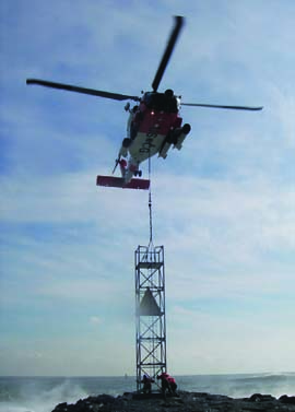 A Coast Guard MH-60 Jayhawk helicopter lowers a 25-foot, 2,540-pound tower to members of Coast Guard Aids to Navigation Team Cape May, N.J., for installation on the north jetty of Shark River Inlet. The previous tower was destroyed by Hurricane Sandy. U.S. Coast Guard Photo by Chief Warrant Officer Christopher Runt